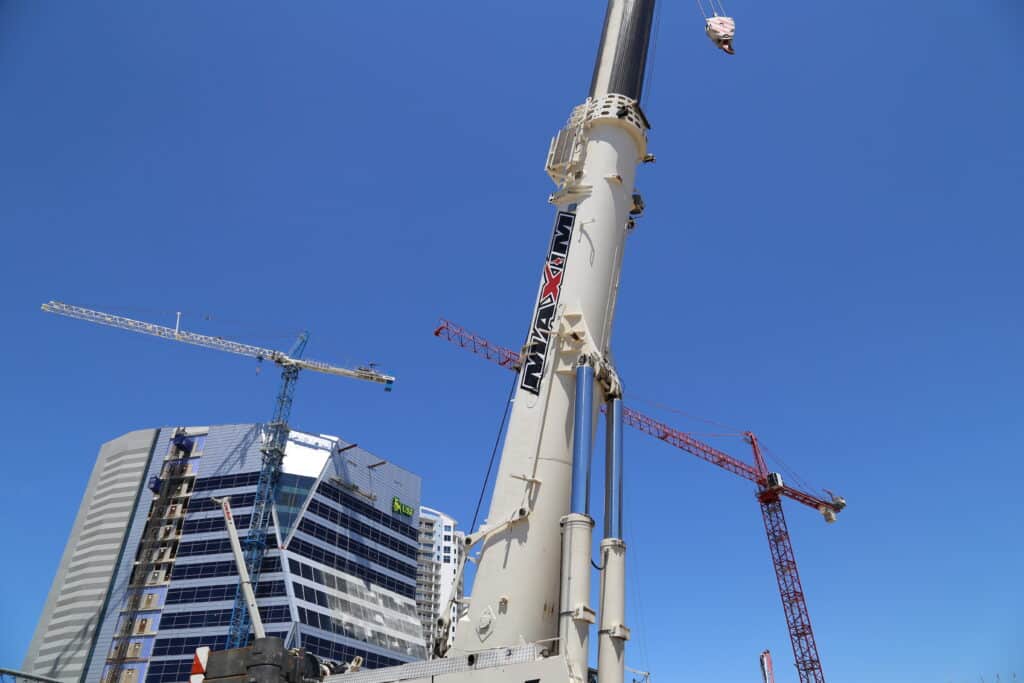 Maxim crane tower crane rentals working on a job site with blue sky and tall building in the background