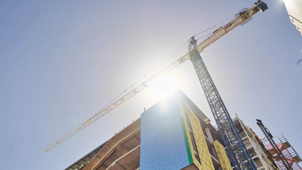 A tower crane over a building with the sun shining through the beams