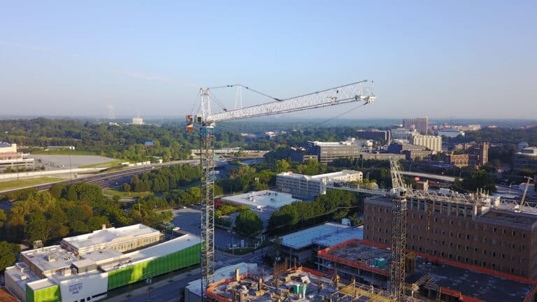 Tower cranes working on a project with a city in the background and lots of foliage.