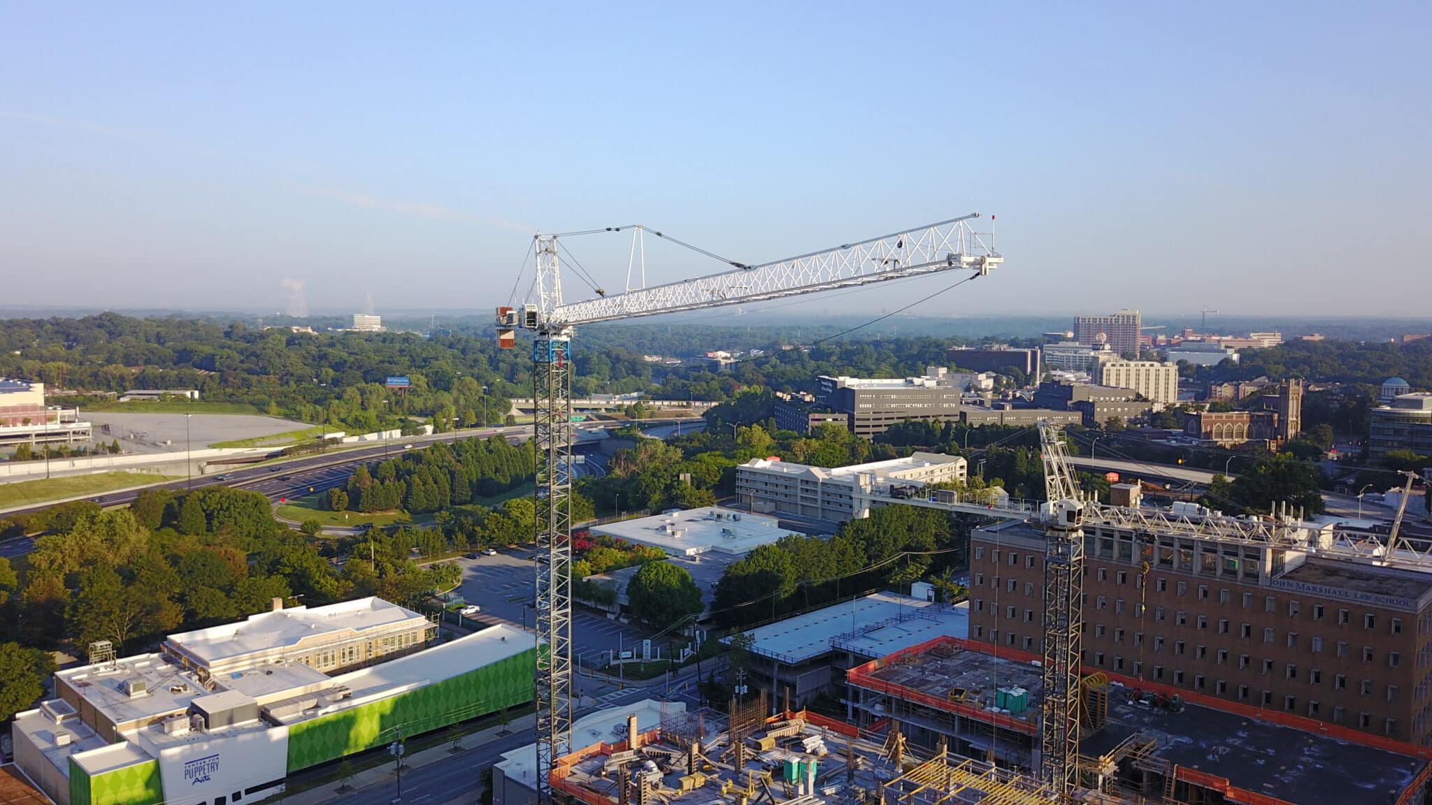 Tower cranes working on a project with a city in the background and lots of foliage.