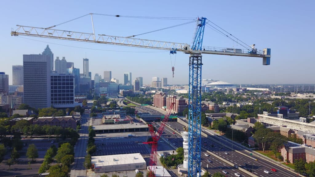 Closeup of a tower crane working on a project with a busy city in the background.