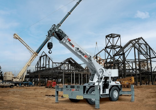 Carry deck crane positioned on a construction site with outriggers extended for stability. Steel frameworks of buildings are visible in the background.