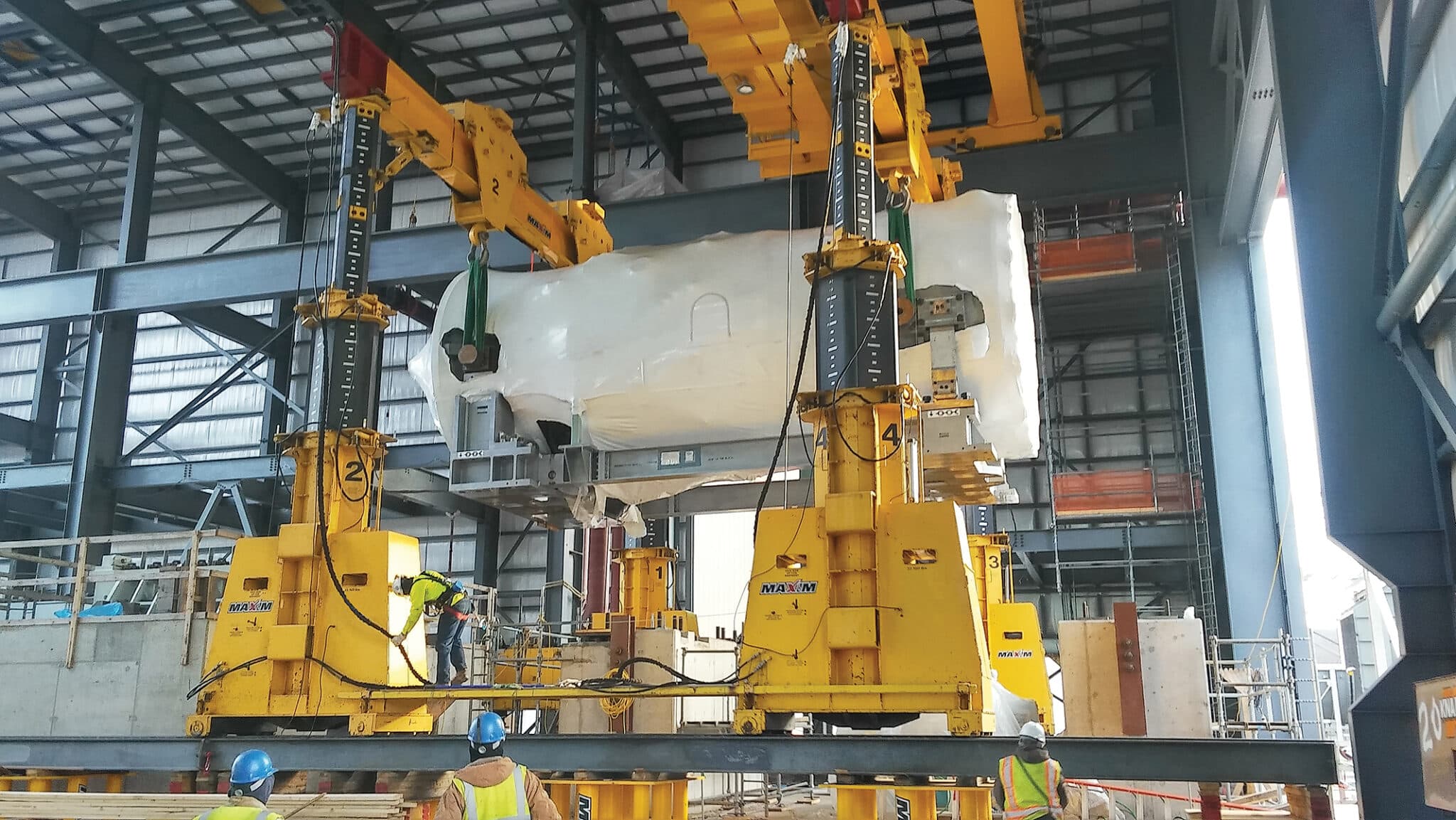 Heavy lifting operation in progress with cranes and skilled workers in a large facility.