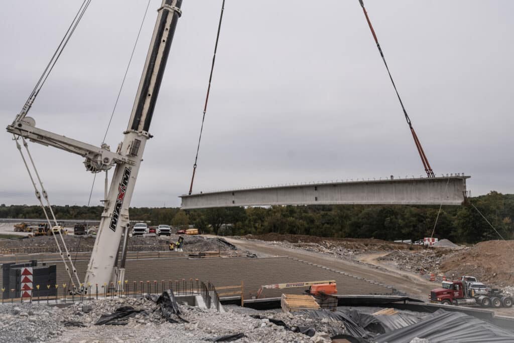 Concrete bridge segment being lifted at a construction site.