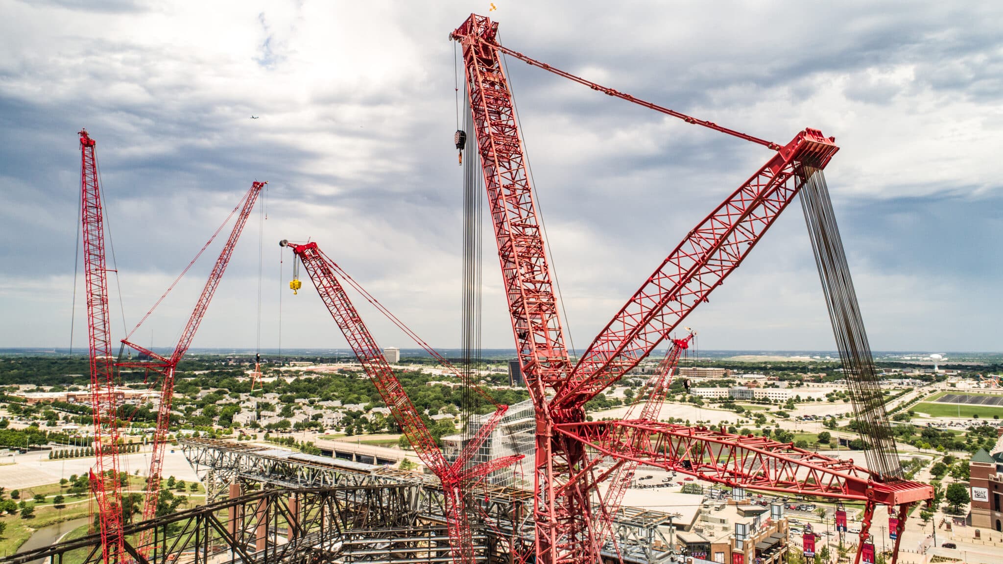 Red construction cranes lift materials over a city landscape, showcasing urban development.