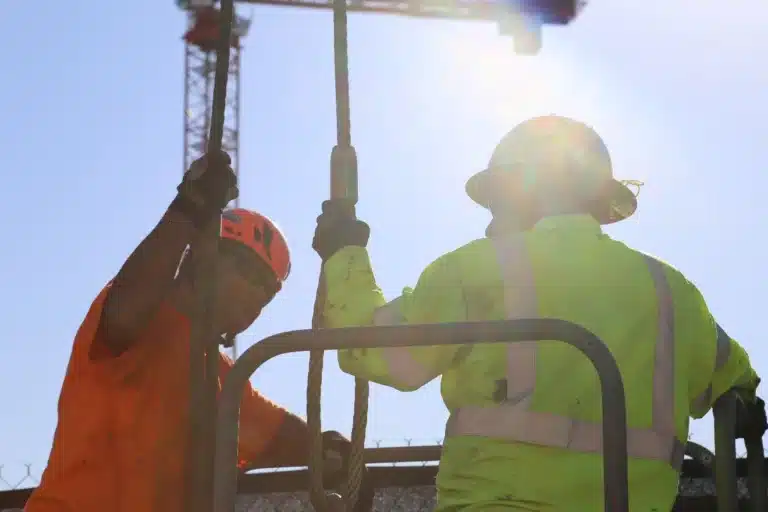 Construction workers using rigging equipment collaborate at sunset, showcasing teamwork and dedication on the job site.
